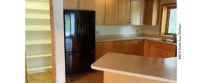 Kitchen with large pantry, black fridge, light wood cabinets, parkay flooring, and stone countertops.