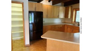Kitchen with large pantry, black fridge, light wood cabinets, parkay flooring, and stone countertops.