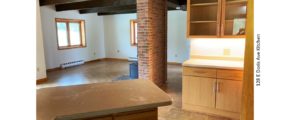 Great room with wood burning fireplace in front of a narrow brick wall, parkay flooring, and kitchen breakfast bar and storage.