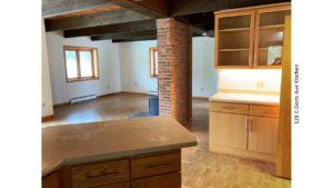 Great room with wood burning fireplace in front of a narrow brick wall, parkay flooring, and kitchen breakfast bar and storage.