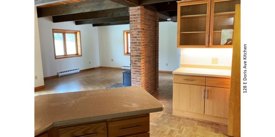 Great room with wood burning fireplace in front of a narrow brick wall, parkay flooring, and kitchen breakfast bar and storage.