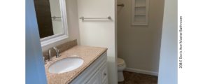 Bathroom with vanity, mirror, and toilet behind a partition wall