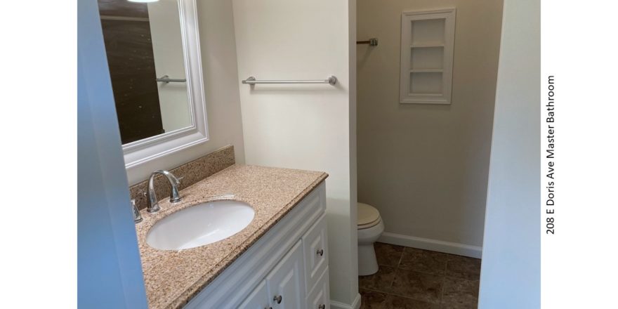 Bathroom with vanity, mirror, and toilet behind a partition wall