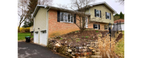 Front exterior of split-level with brick, horizontal siding, black shutters, bay-window and landscaping.