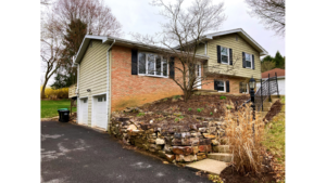 Front exterior of split-level with brick, horizontal siding, black shutters, bay-window and landscaping.