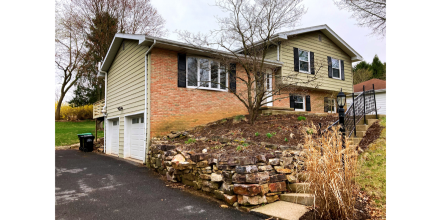 Front exterior of split-level with brick, horizontal siding, black shutters, bay-window and landscaping.