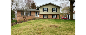 Exterior of a split-level house with brick and siding exterior and black shutters. Front yard is a hill with steps leading up from the driveway to the front door.