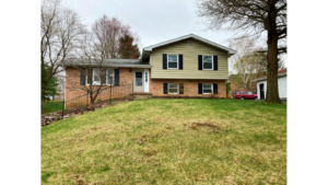 Exterior of a split-level house with brick and siding exterior and black shutters. Front yard is a hill with steps leading up from the driveway to the front door.