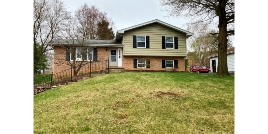 Exterior of a split-level house with brick and siding exterior and black shutters. Front yard is a hill with steps leading up from the driveway to the front door.