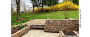 Sunken patio with fire pit. Lawn with trees and flower bushes.