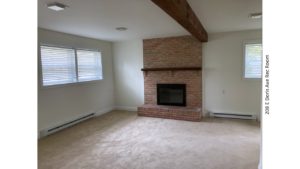 Carpeted rec room with exposed beam and brick fireplace with mantle