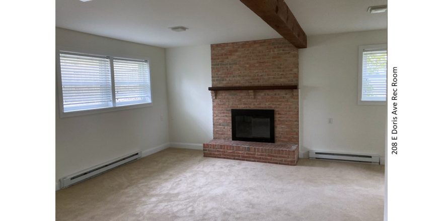 Carpeted rec room with exposed beam and brick fireplace with mantle