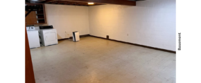 a large basement with white walls and wood beams on the ceiling and a washer and dryer unit