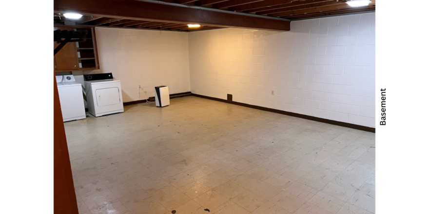 a large basement with white walls and wood beams on the ceiling and a washer and dryer unit