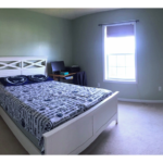 Carpeted bedroom with full-size bed, desk, and small nightstand with lamp