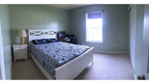 Carpeted bedroom with full-size bed, desk, and small nightstand with lamp