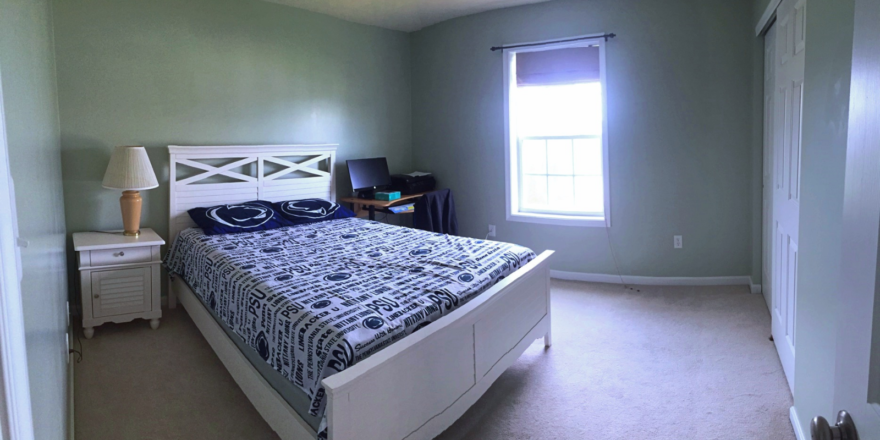 Carpeted bedroom with full-size bed, desk, and small nightstand with lamp