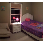 Carpeted bedroom with full-size bed, armchair, and small dresser with lamp