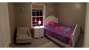 Carpeted bedroom with full-size bed, armchair, and small dresser with lamp