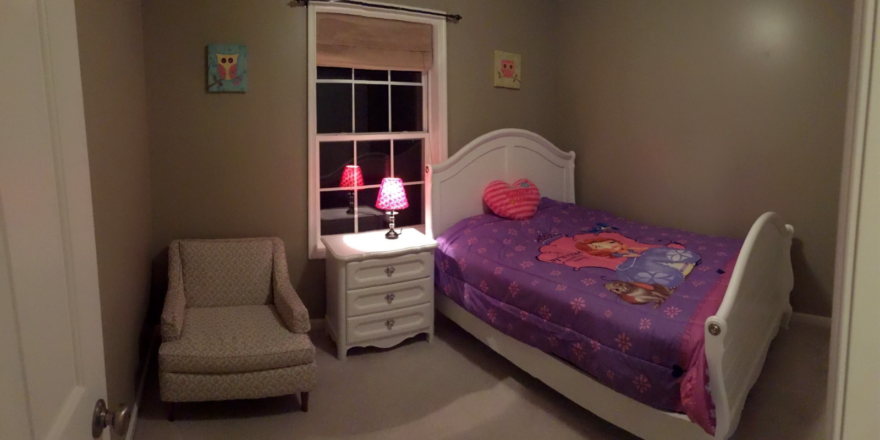 Carpeted bedroom with full-size bed, armchair, and small dresser with lamp