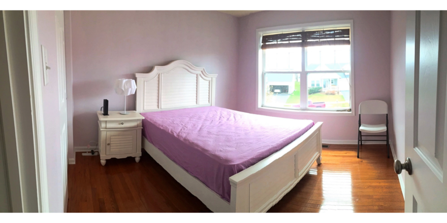 Bedroom with hardwood floor and full size bed, nightstand with lamp, and small chair