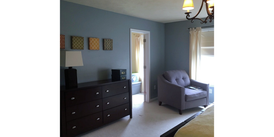 Carpeted bedroom with armchair and dresser and chandelier