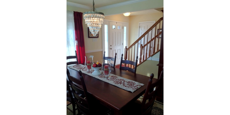 Entryway with wooden staircase and dining room with large table and chandelier
