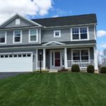 Exterior of two story house with gray siding, large yard, driveway, and front porch