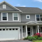 Exterior of two story house with gray siding, large yard, driveway, and front porch