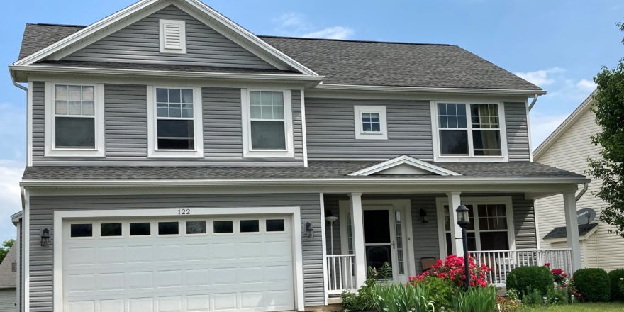 Exterior of two story house with gray siding, large yard, driveway, and front porch