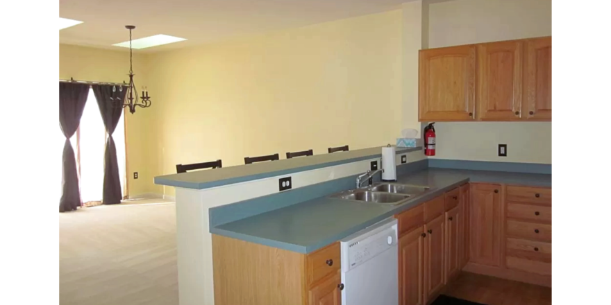 Kitchen and dining area with wood-tone cabinets, double bowl sink, dishwasher, and bar stool seating