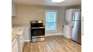 Kitchen with window, pale blue counters, wood-style flooring, stainless steel range oven and refrigerator and white stackable washer/dryer