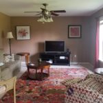 Carpeted family room with seating, accent tables, television and ceiling fan