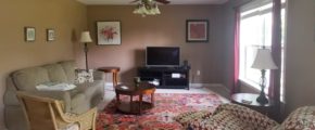 Carpeted family room with seating, accent tables, television and ceiling fan