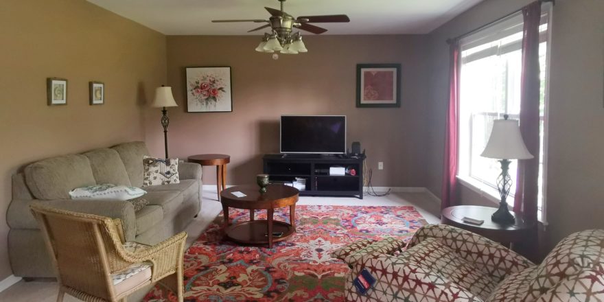 Carpeted family room with seating, accent tables, television and ceiling fan