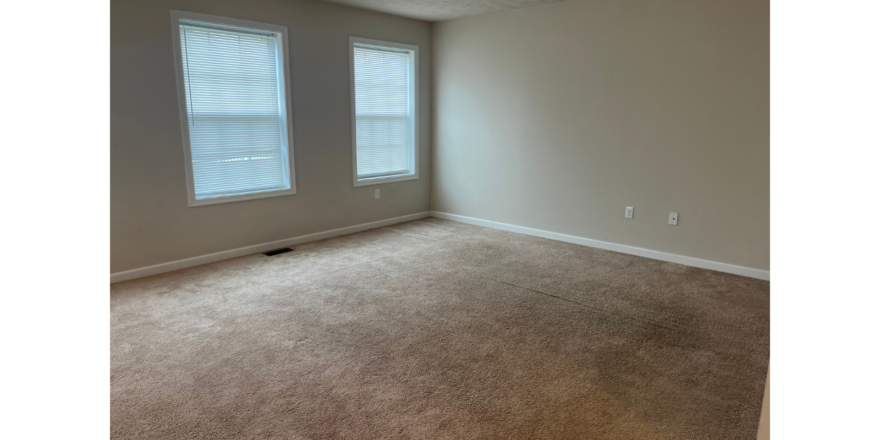 an empty room with a carpeted floor and two windows