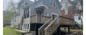 Back of property with stairs leading to a deck, gray siding and windows with white trim