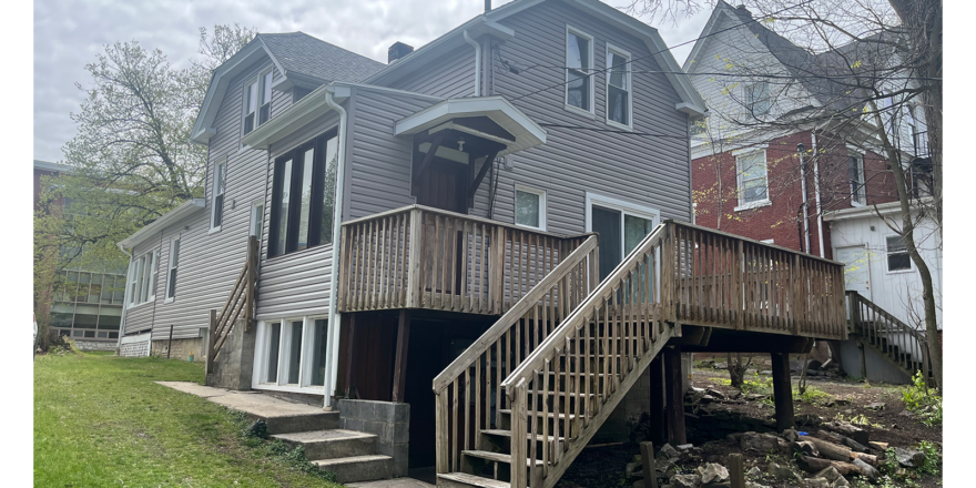 Back of property with stairs leading to a deck, gray siding and windows with white trim