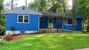 Exterior of ranch house with bright blue siding and front yard.