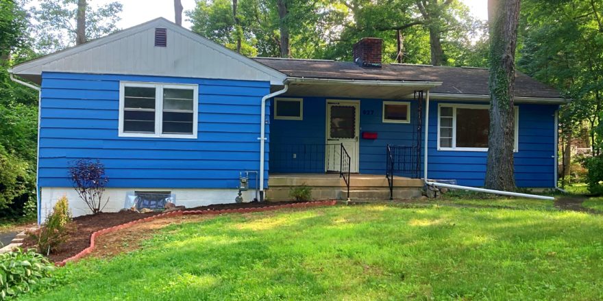 Exterior of ranch house with bright blue siding and front yard.