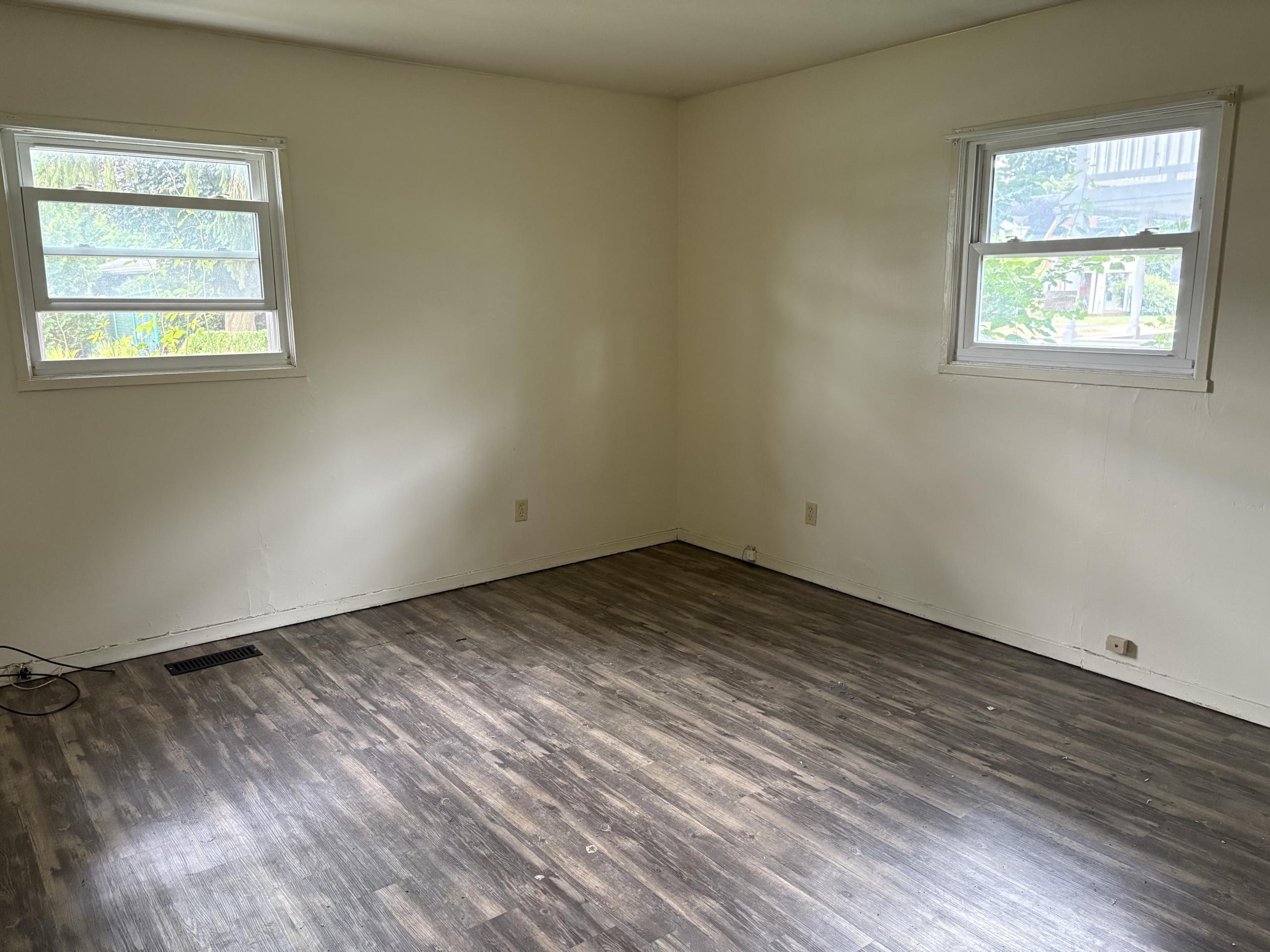 Empty room with two windows and dark wood floor