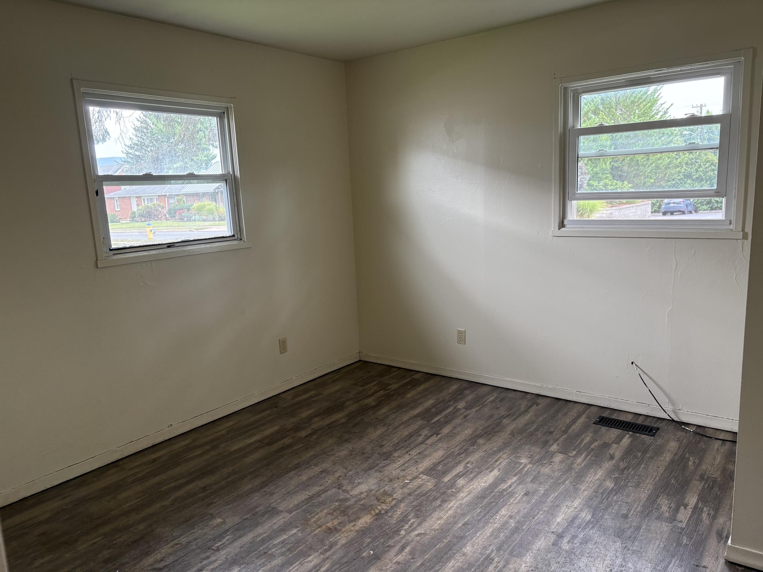 Empty room with two windows and wood floor.