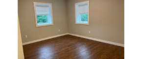 an empty room with two windows and a hard wood floor