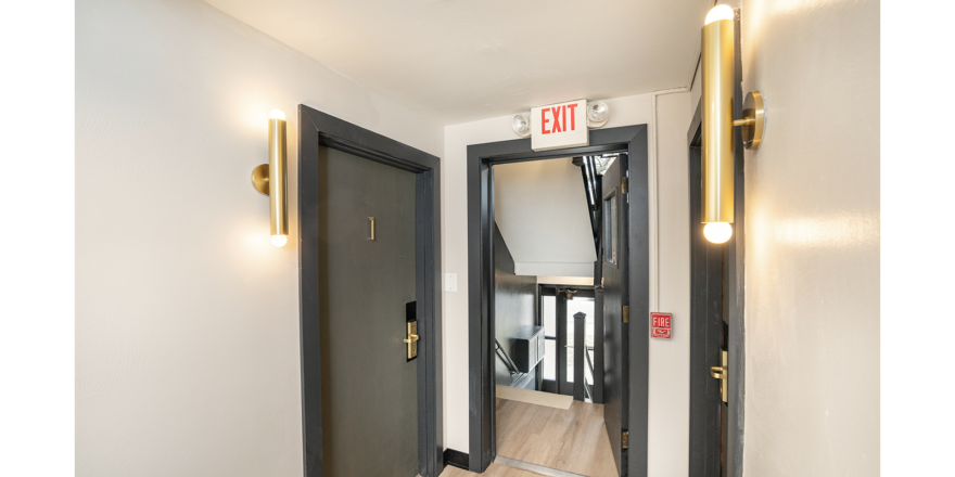 a hallway with two doors and a red exit sign