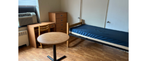 a small room with a bed, desk, and cabinet