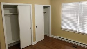 Bedroom with two closets, window, and laminate, hardwood-style flooring
