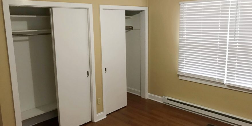 Bedroom with two closets, window, and laminate, hardwood-style flooring