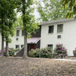 back exterior of galenwood showing a white painted building surrounded by trees, flowers and bushes
