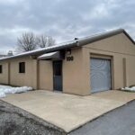 a tan building with a garage and snow on the ground