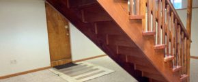 Basement den with carpet and wooden stairwell in the middle of the room